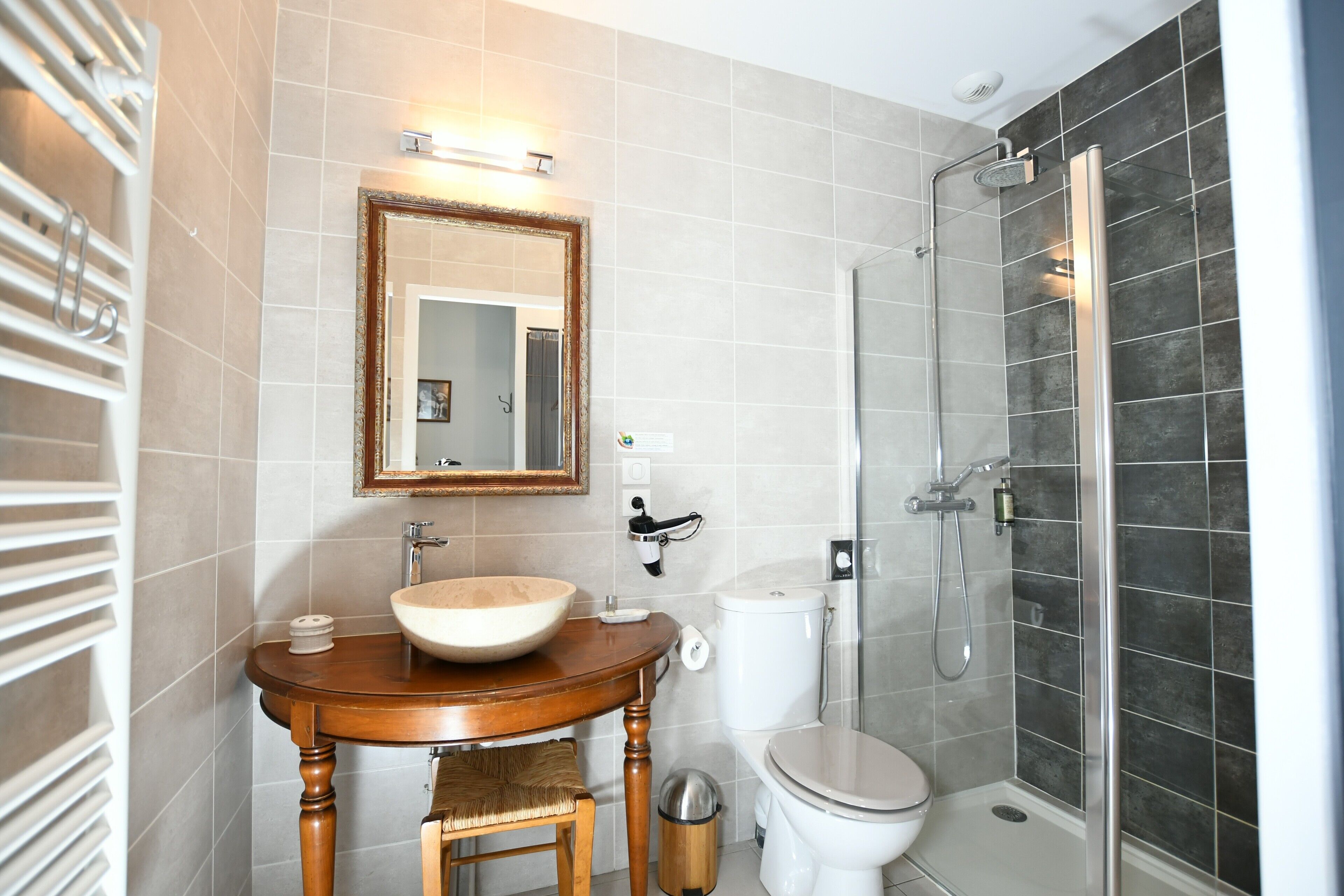 Een badkamer met een houten wastafelmeubel, een grote spiegel, een toilet en een douche met glazen wanden.