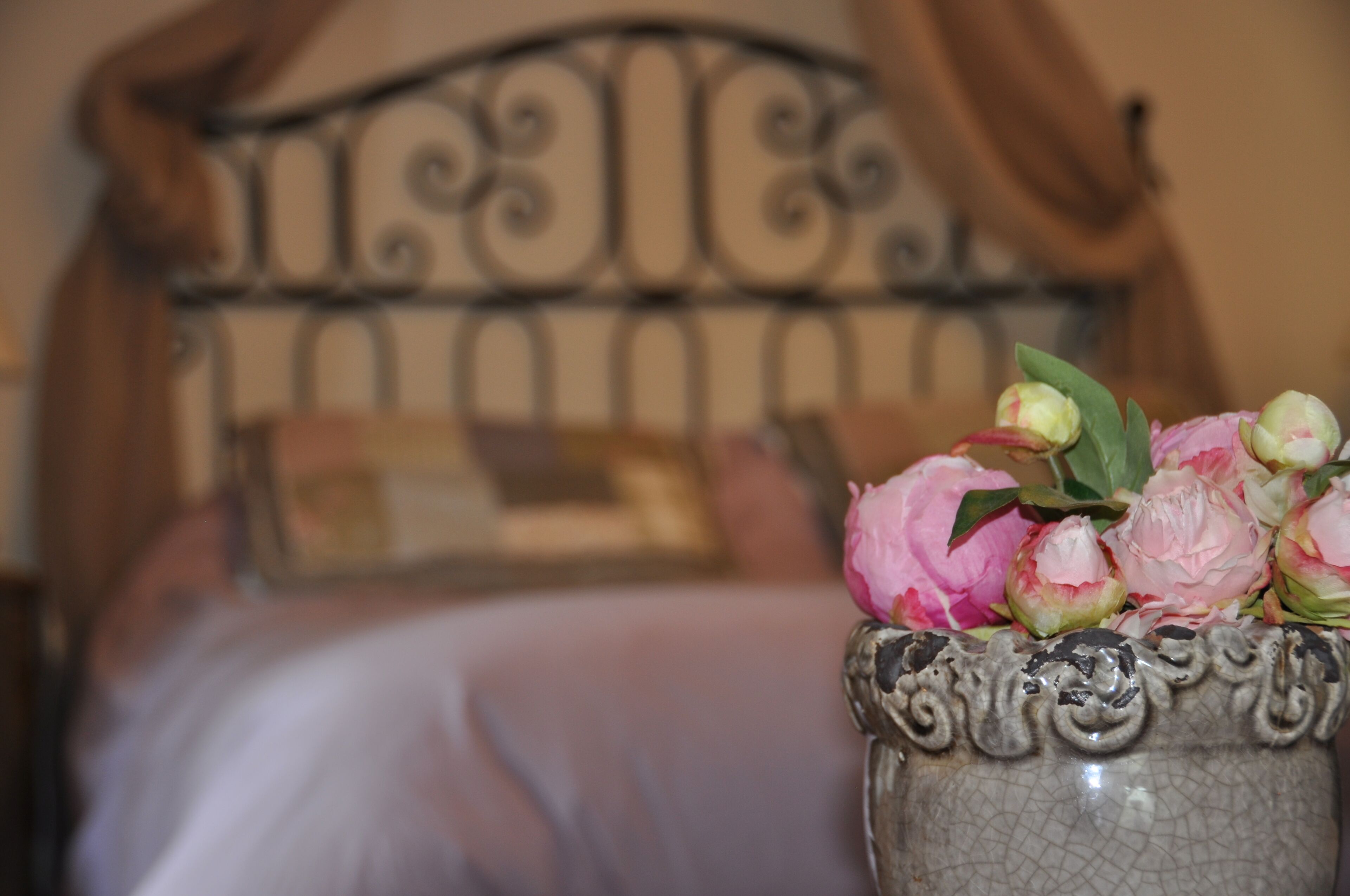 Una cama con cabecera de metal y un florero con flores sobre una mesita de noche.