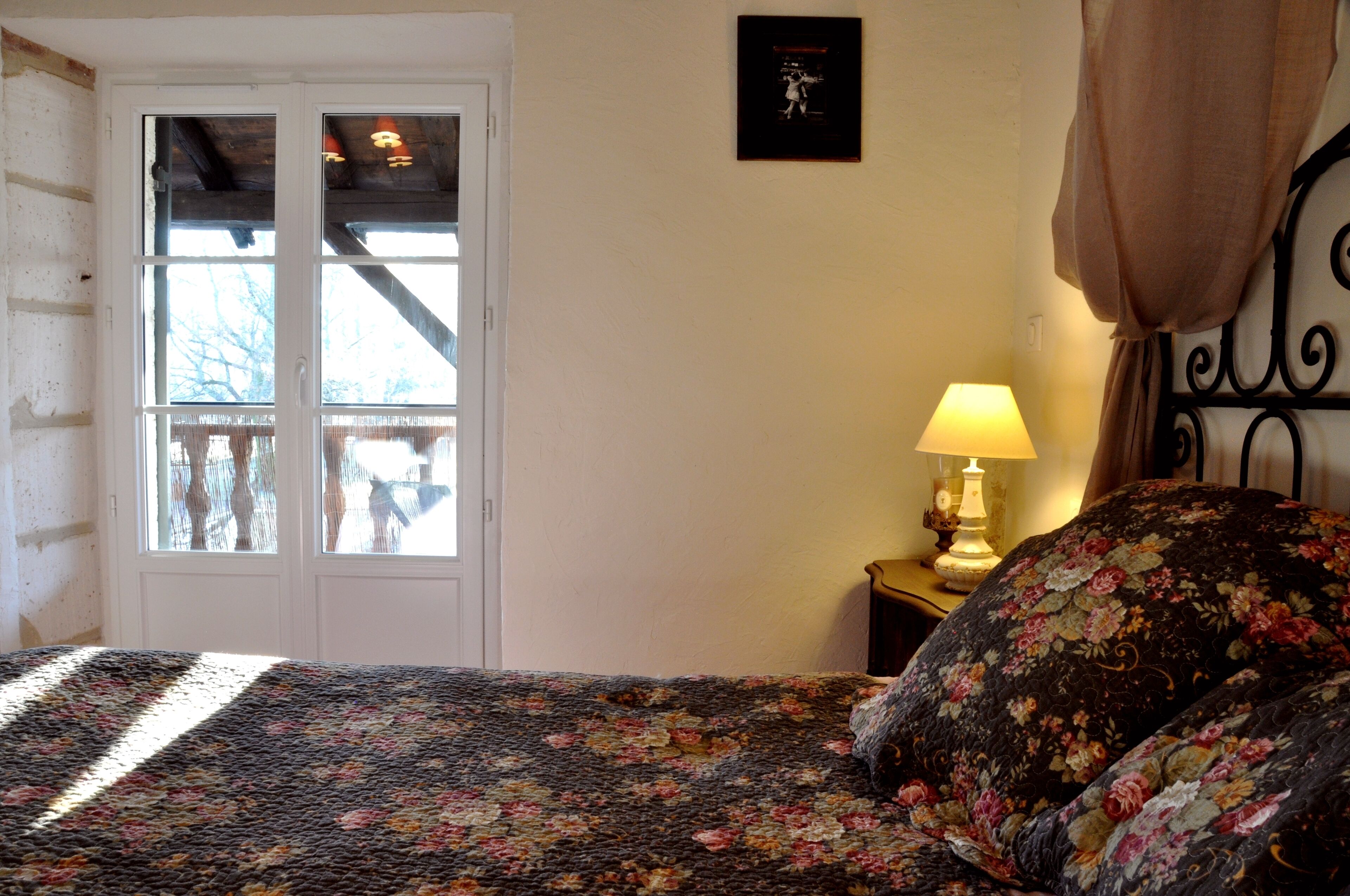 Un dormitorio con cama, ventana, lámpara y un cuadro en la pared.
