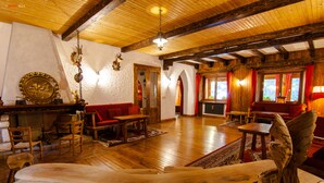 A spacious room with wooden floors, red sofas, a wooden table, and a decorative bird sculpture. - Hotel Mille Pini (Scanno)
