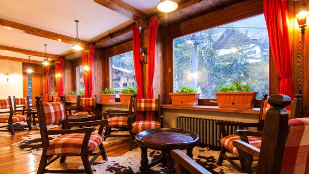 A cozy interior with wooden furniture, red curtains, and potted plants. - Hotel Mille Pini (Scanno)