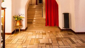 A hallway with a wooden floor, an arched ceiling, a staircase with red curtains, and a vase with flowers on a side table. - Hotel Mille Pini (Scanno)