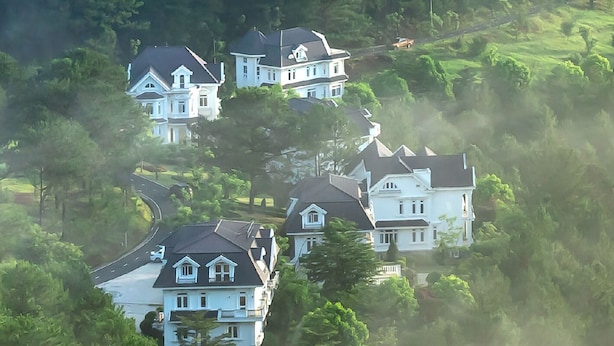 A cluster of large, white houses with dark roofs, surrounded by lush greenery and a winding road. - Sam Tuyen Lam Resort (Xuan Huong - Da Lat)