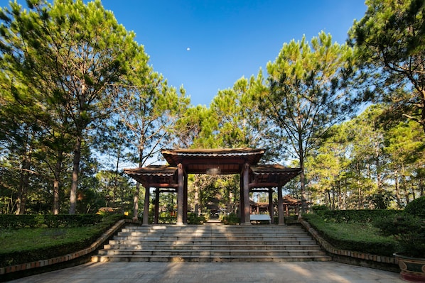 A traditional wooden pavilion with a tiled roof, surrounded by lush greenery and pine trees.