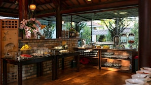 A buffet setup with various food items and beverages, a brick wall, and a view through large windows. - Sam Tuyen Lam Resort (Xuan Huong - Da Lat)
