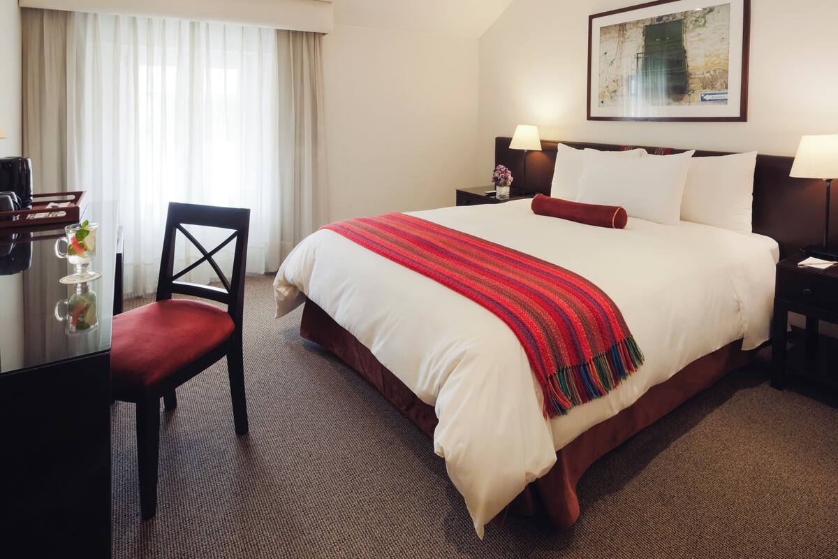A hotel room with a large bed, a desk with a chair, and a window with curtains.