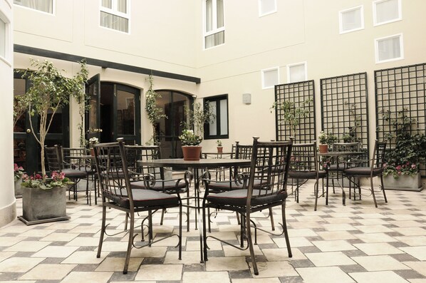 A courtyard with a checkered floor, outdoor seating with metal chairs and tables, potted plants, and a building with multiple windows and doors. - LP Los Portales Hotel Cusco (Cusco)