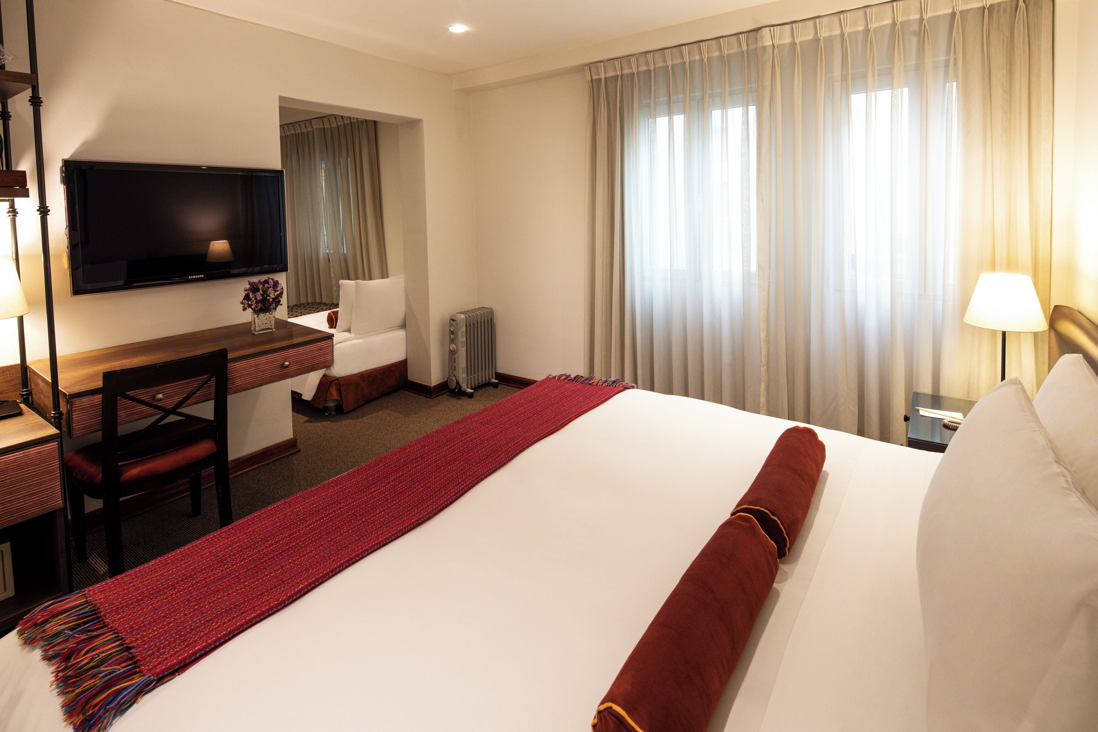Una habitación de hotel con una cama grande, un escritorio con silla, un televisor y una ventana con cortinas.