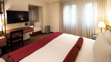 Una habitación de hotel con una cama grande, un escritorio con silla, un televisor y una ventana con cortinas.