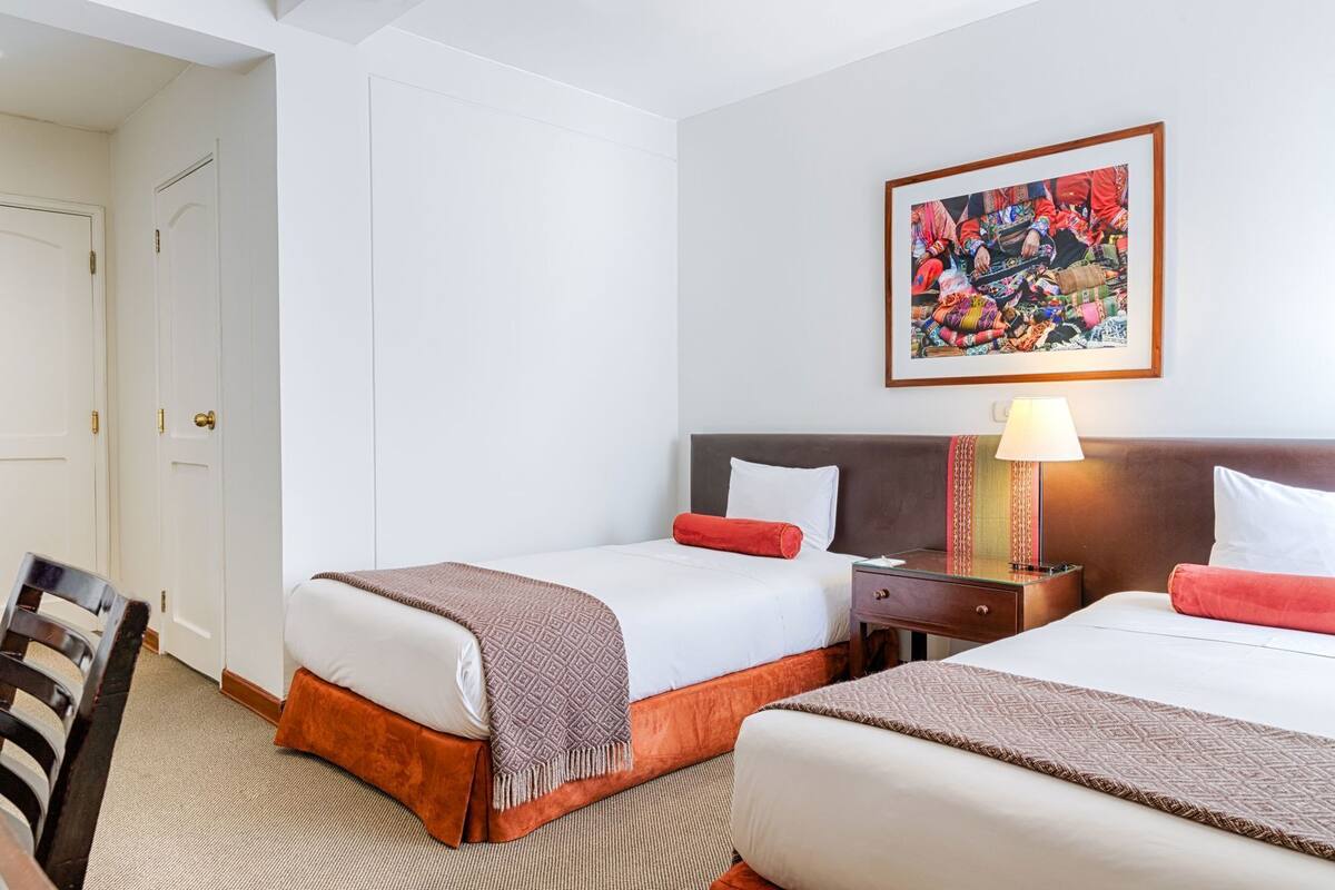 A hotel room with two beds, a nightstand with a lamp, a framed picture on the wall, and a chair.