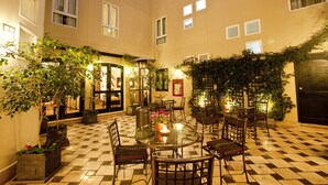 A courtyard with a glass table surrounded by chairs, potted plants, and a checkered floor. - LP Los Portales Hotel Cusco (Cusco)