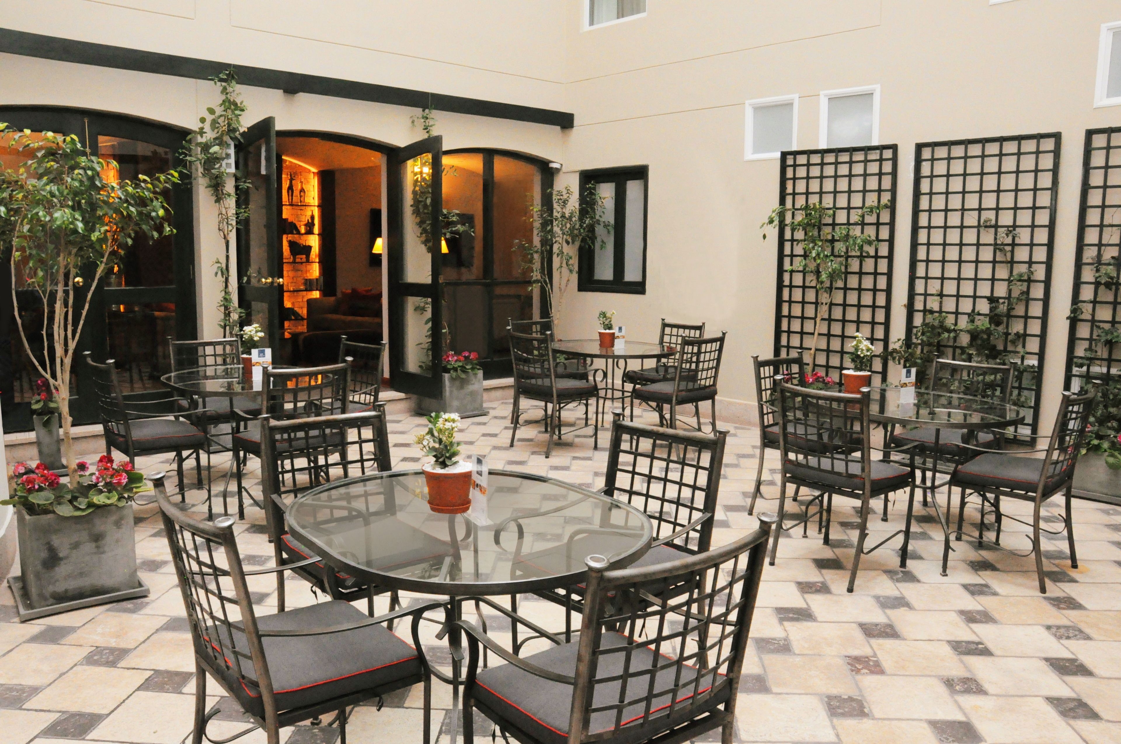 An outdoor patio with round tables and chairs, surrounded by potted plants and a tiled floor.