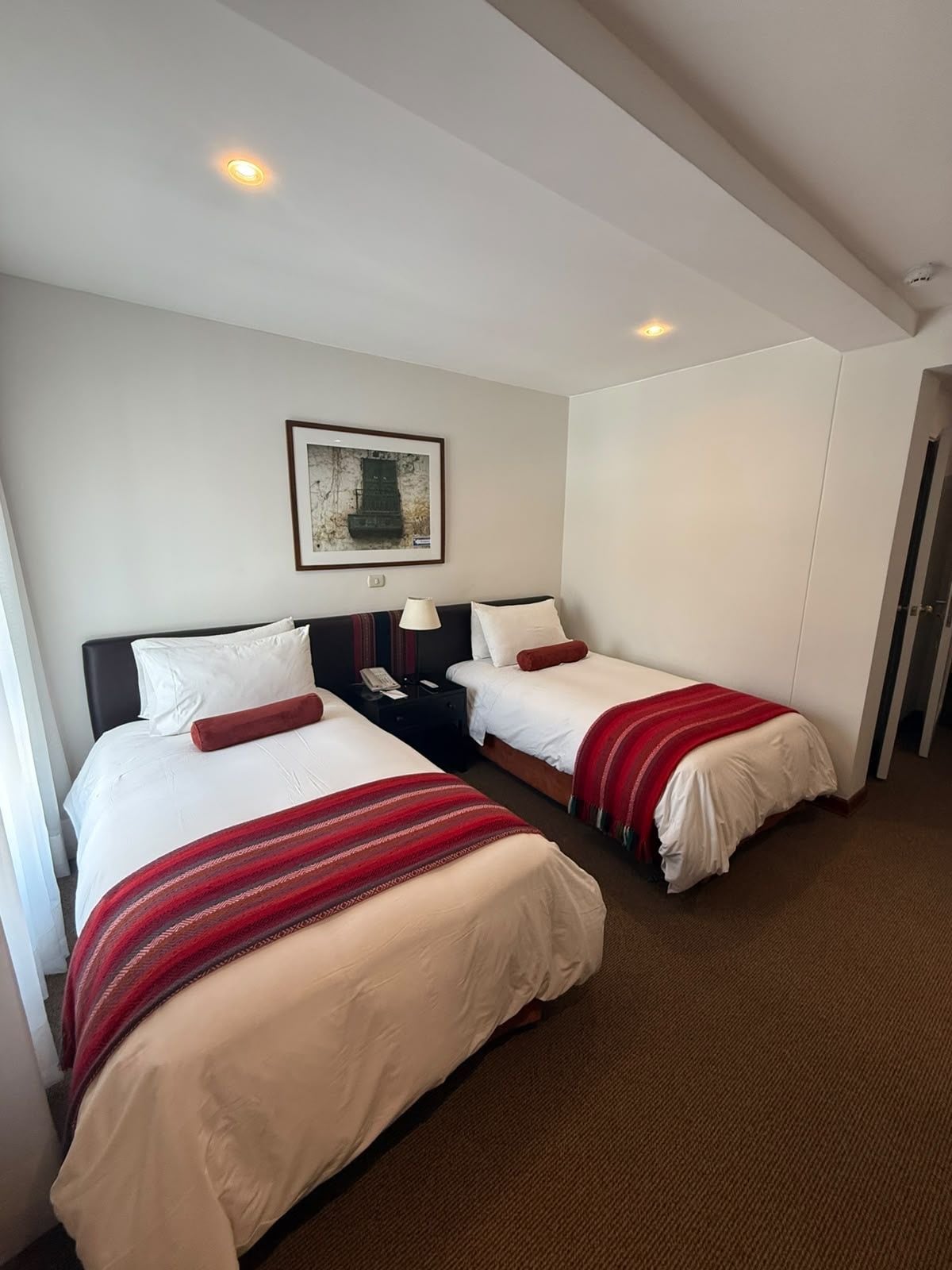 Habitación de hotel con dos camas, un cuadro en la pared y una puerta a la derecha.