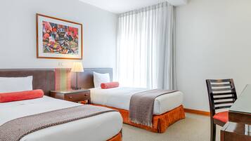 Een hotelkamer met twee bedden, een bureau, een stoel, een lamp en een groot raam met gordijnen.