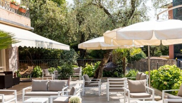 An outdoor patio with white furniture, including sofas and chairs, and large umbrellas providing shade. - Hotel Pace (Torri del Benaco)
