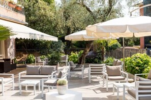 An outdoor patio with white furniture, including sofas and chairs, and large umbrellas providing shade. - Hotel Pace (Torri del Benaco)