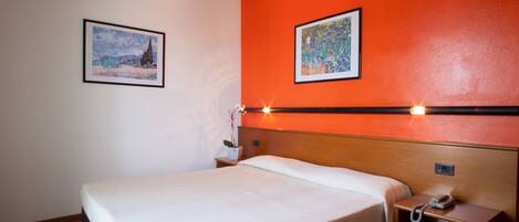 Habitación de hotel con cama, mesita de noche con teléfono y dos cuadros en la pared.