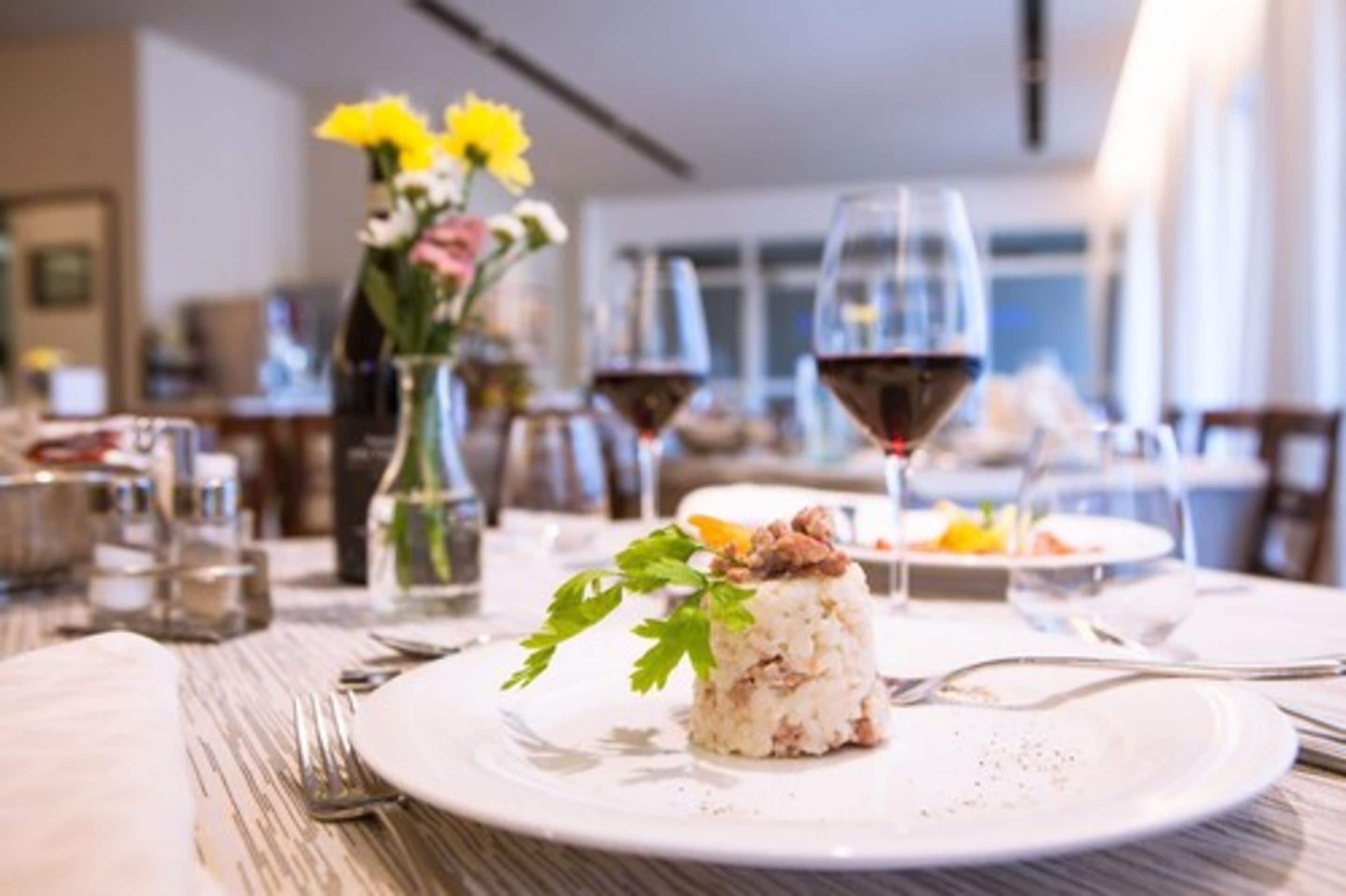 A dining table with a plate of food, wine glasses, and a vase of flowers.