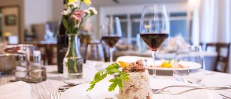 A dining table with a plate of food, wine glasses, and a vase of flowers.