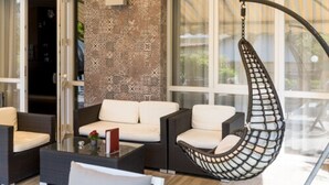 A modern living room with a hanging chair, white sofas, and a glass coffee table. - Hotel Pace (Torri del Benaco)