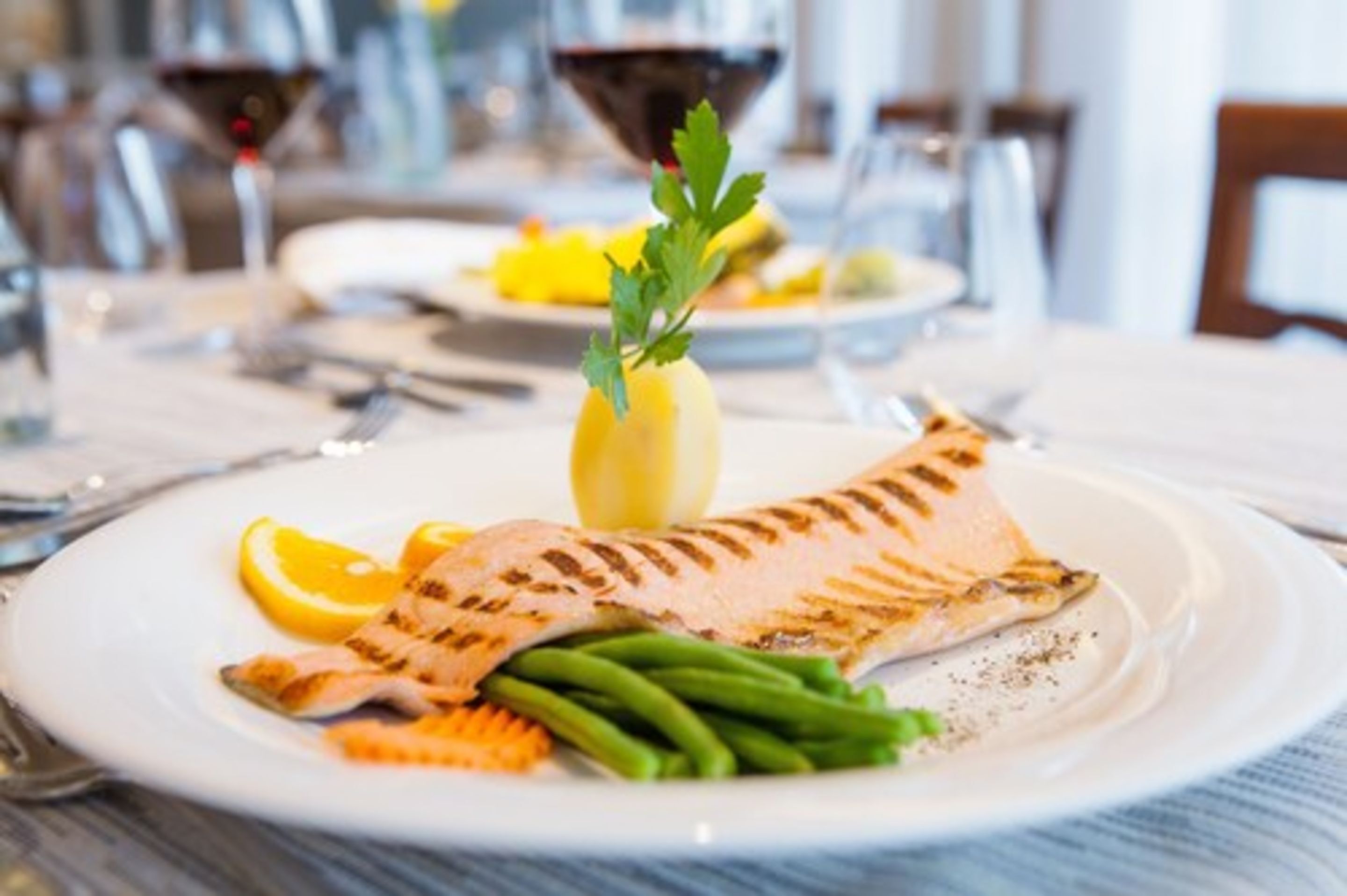 A plate with grilled fish, green beans, lemon, and a garnish on a white plate.
