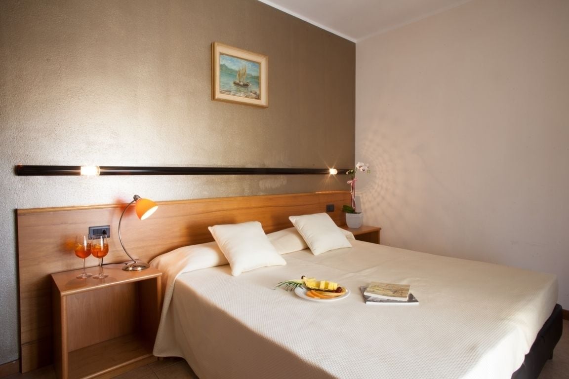 A neatly made bed with a headboard, a bedside table with a lamp, and a plate of fruit on the bed.