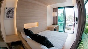 A modern hotel room with a curved ceiling, a large bed with a black pillow, a bedside table, a lamp, and a window offering a view of the outside. - Sleepbox Chiangmai Hotel (Chiang Mai)