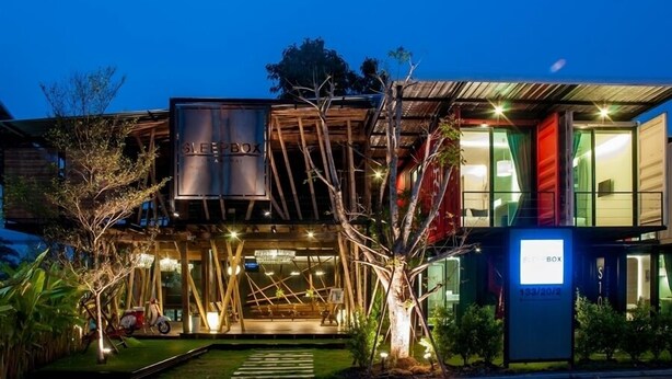 A modern building with a prominent 'SLEEPBOX' sign, large windows, and a well-lit entrance area with outdoor seating. - Sleepbox Chiangmai Hotel (Chiang Mai)