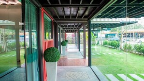 A covered walkway with glass doors, a red door, and a green hedge. - Sleepbox Chiangmai Hotel (Chiang Mai)