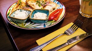 A plate with toast, a red pepper, and two small bowls of white and blue sauces, accompanied by a fork and knife on a yellow napkin. - TL Hotel Budapest (Budapest)