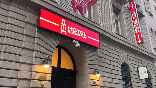 A hotel facade with a prominent red sign, a large arched entrance, and multiple windows. - TL Hotel Budapest (Budapest)