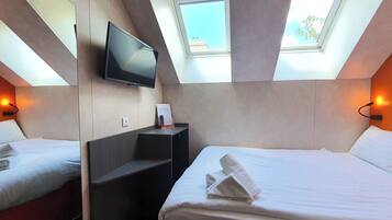 Habitación de hotel con cama, televisor montado en la pared, una mesita y ventana con vista al cielo.