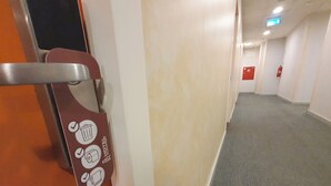 A hallway with a door handle, a fire extinguisher, and a sign with icons. - TL Hotel Budapest (Budapest)
