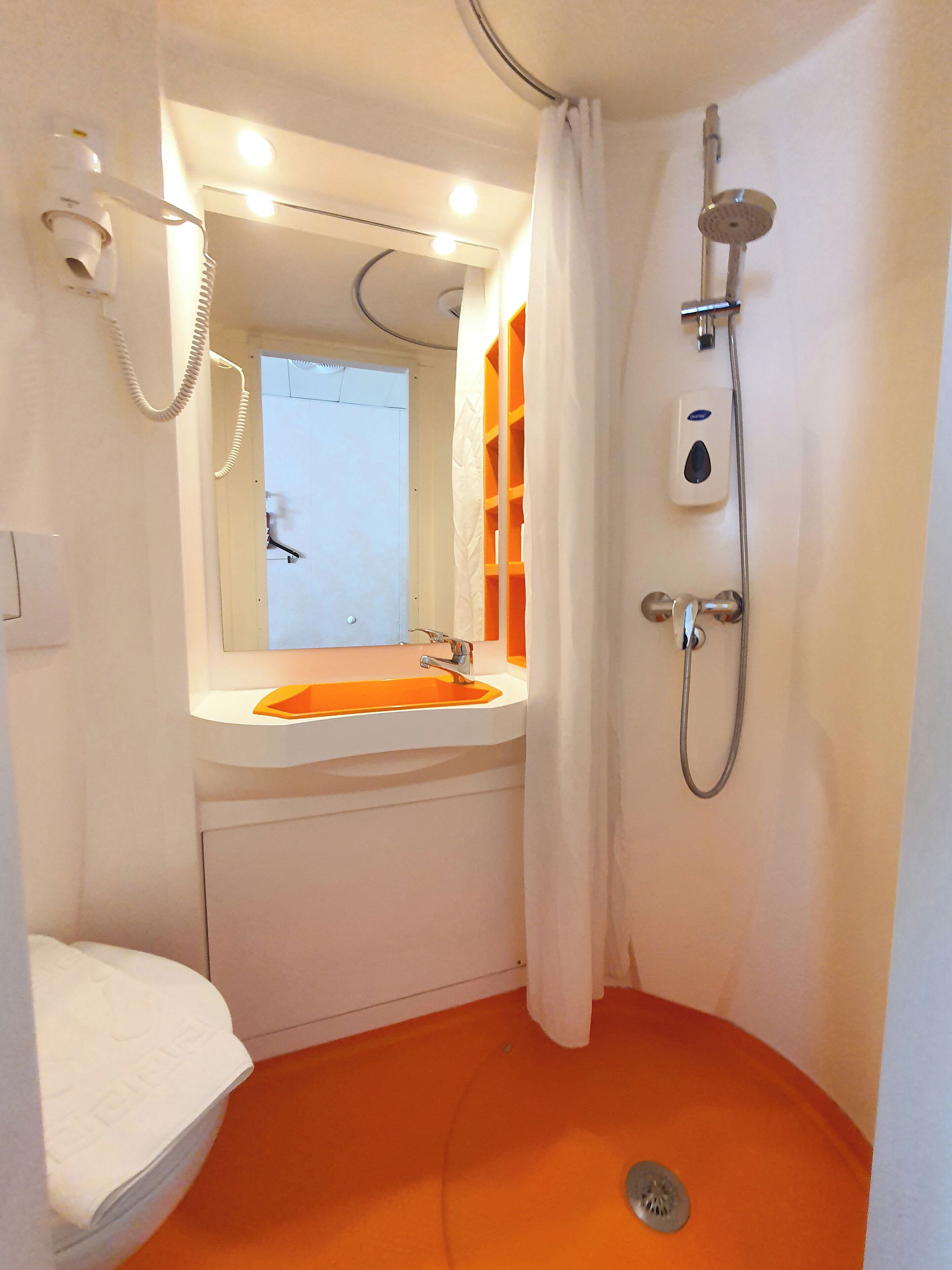 Ein Badezimmer mit weißem Waschbecken, einem Spiegel, einer Dusche mit Duschbrause und einer Toilette.