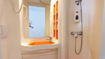 Ein Badezimmer mit weißem Waschbecken, einem Spiegel, einer Dusche mit Duschbrause und einer Toilette.