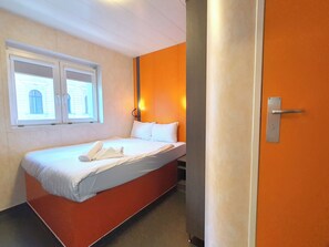 A hotel room with a bed, a window, and an orange wall. - TL Hotel Budapest (Budapest)