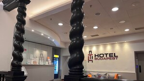 A hotel lobby with a modern design, featuring a reception desk, a wall-mounted sign for the hotel, and a staircase with decorative balusters. - TL Hotel Budapest (Budapest)
