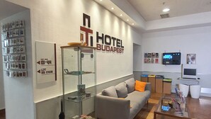 A hotel lobby with a reception desk, a sofa, a coffee table, and a glass display case. - TL Hotel Budapest (Budapest)