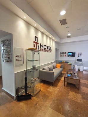 Un vestíbulo de hotel con una recepción, un sofá, una mesa de centro y una vitrina de vidrio.