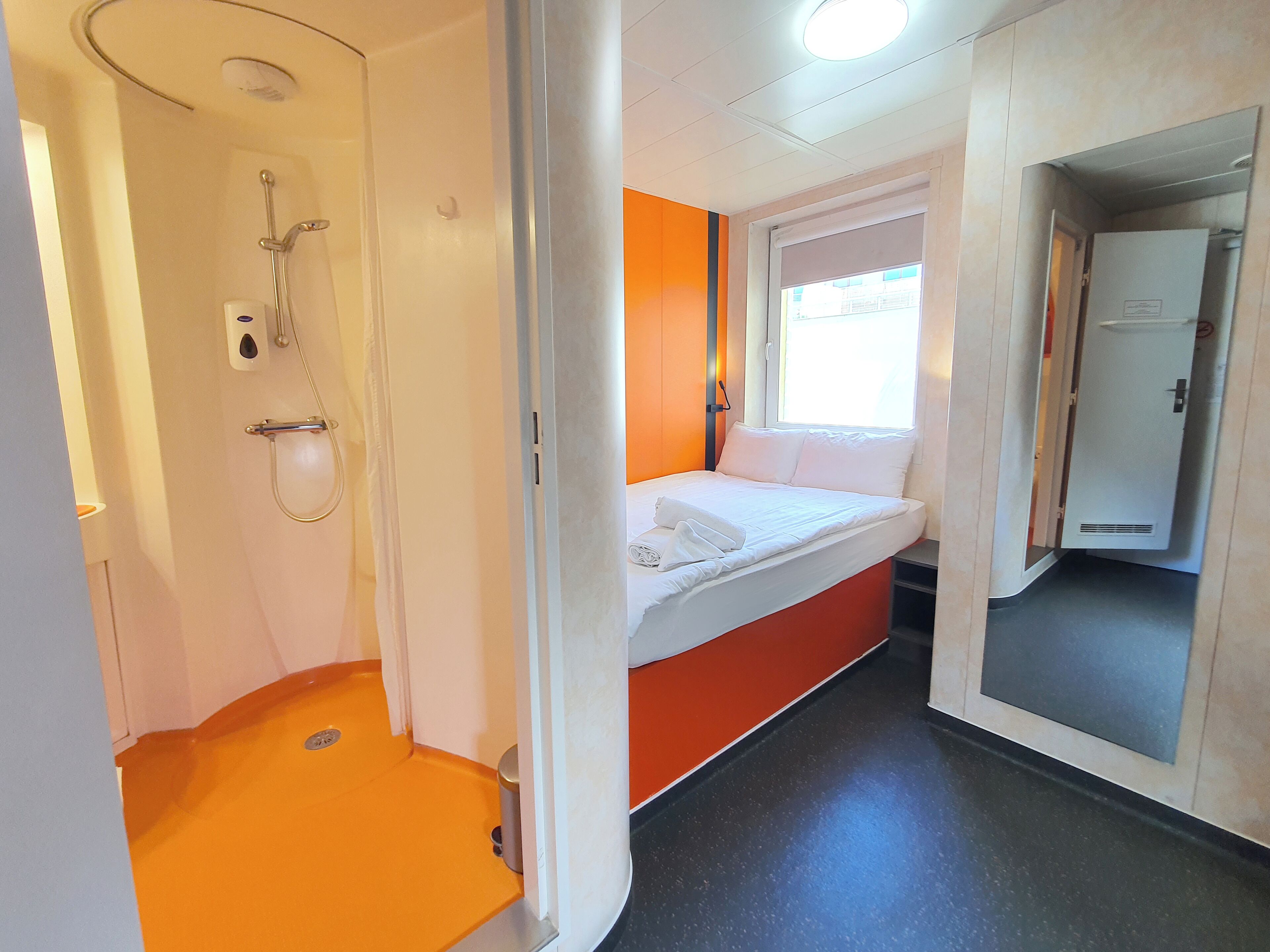 Habitación de hotel pequeña con ducha, cama y ventana.
