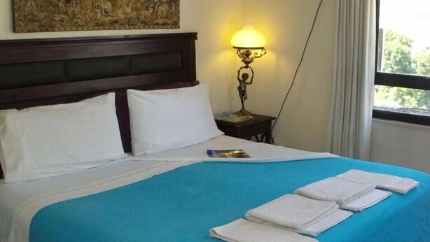 Een hotelkamer met een groot bed, een nachtkastje met lamp, een schilderij aan de muur en een raam met gordijnen.