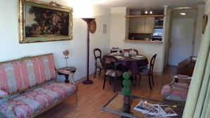Een woonkamer met een bank, een eettafel met stoelen, een glazen salontafel, en een schilderij aan de muur.