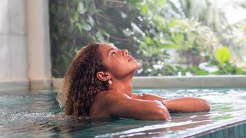 A person in a pool with clear water, surrounded by greenery.