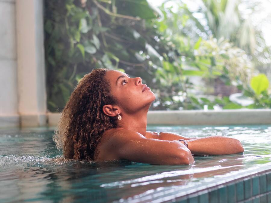 A person in a pool with clear water, surrounded by greenery.