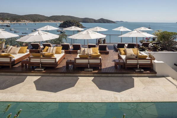 Terraza con tumbonas y sombrillas con vistas a un cuerpo de agua y barcos.