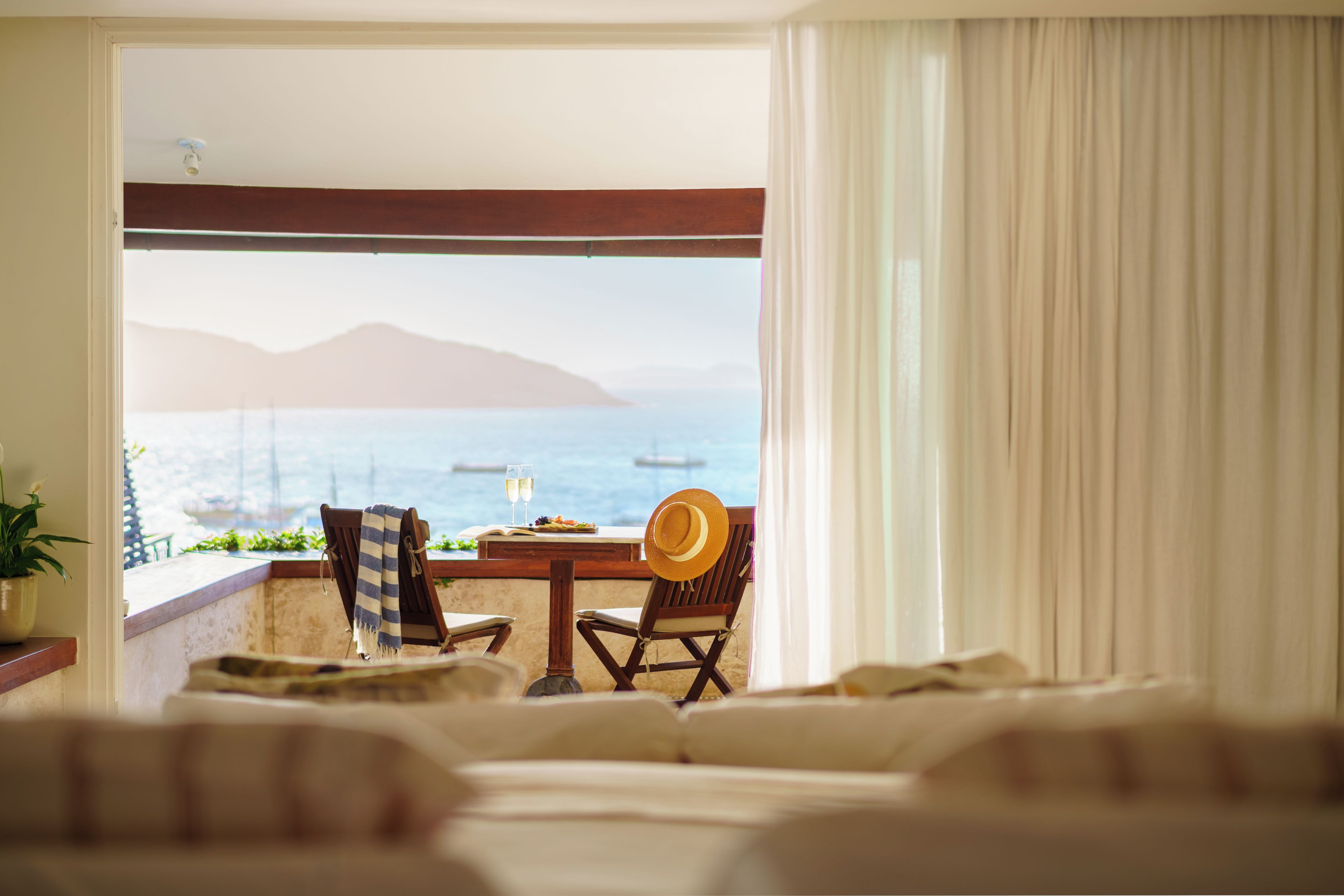 A room with a view of the sea, a dining table with chairs, and a bed.
