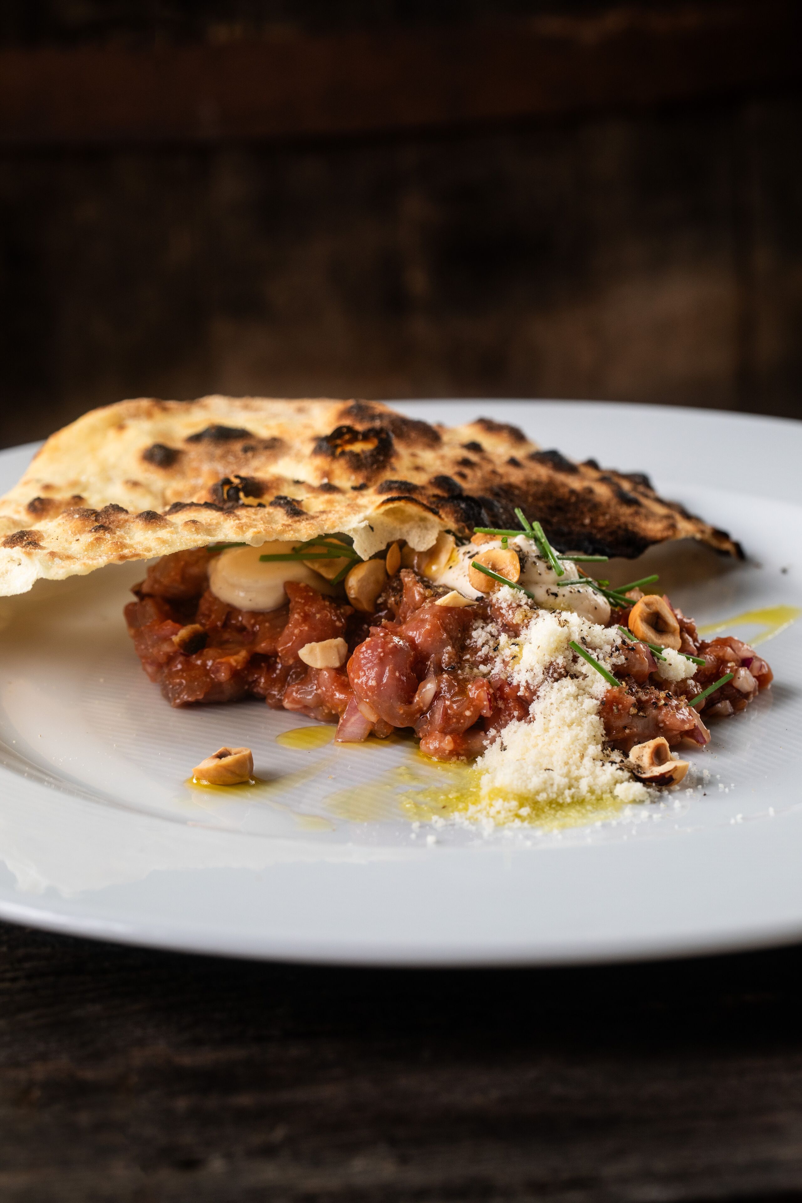 A plate with a dish of meat and vegetables, topped with herbs and nuts, and a piece of flatbread.