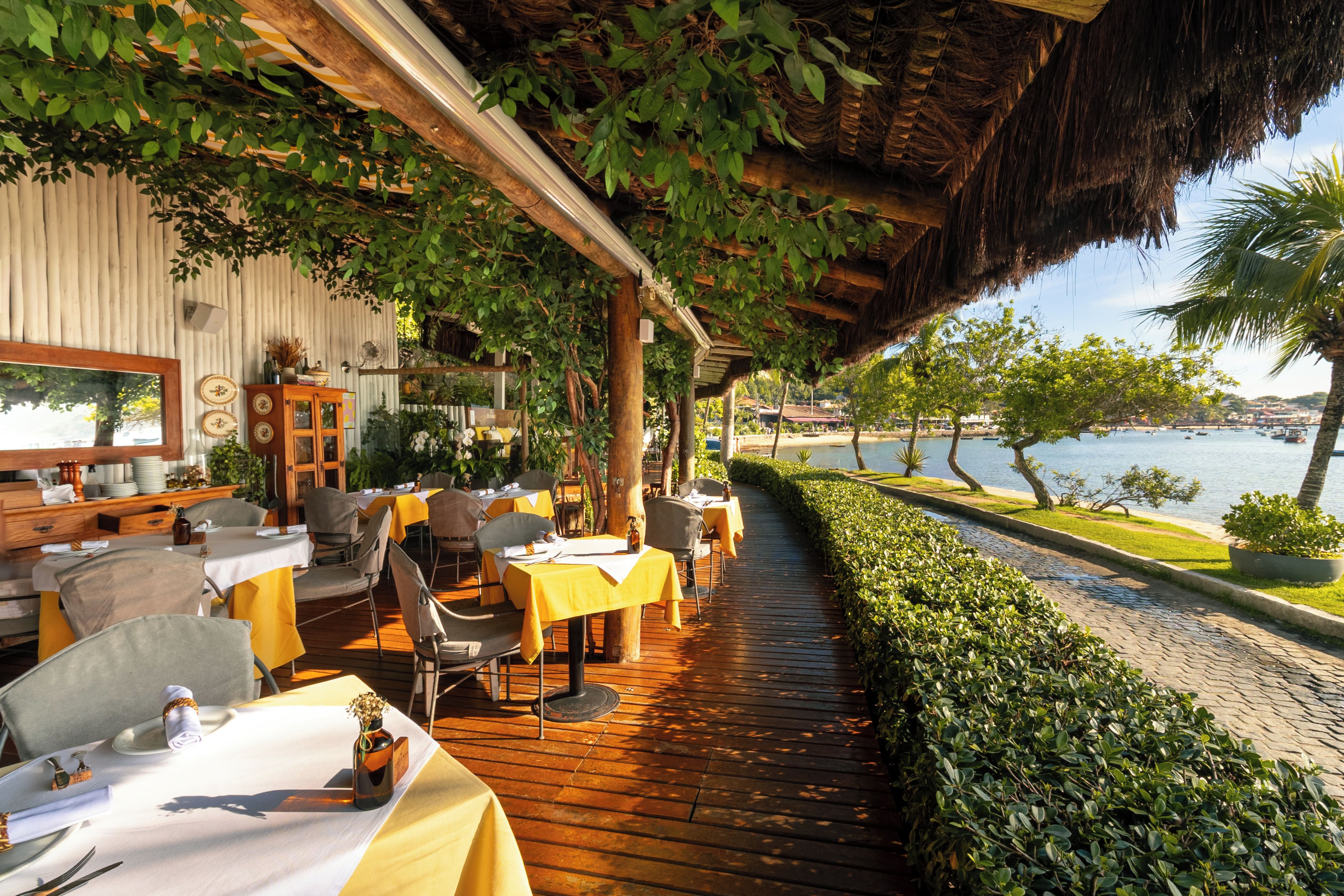 An outdoor dining area with tables and chairs, a wooden deck, and a view of the water.