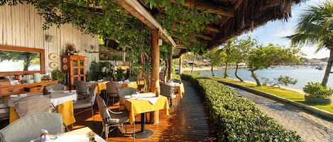 An outdoor dining area with tables and chairs, a wooden deck, and a view of the water.