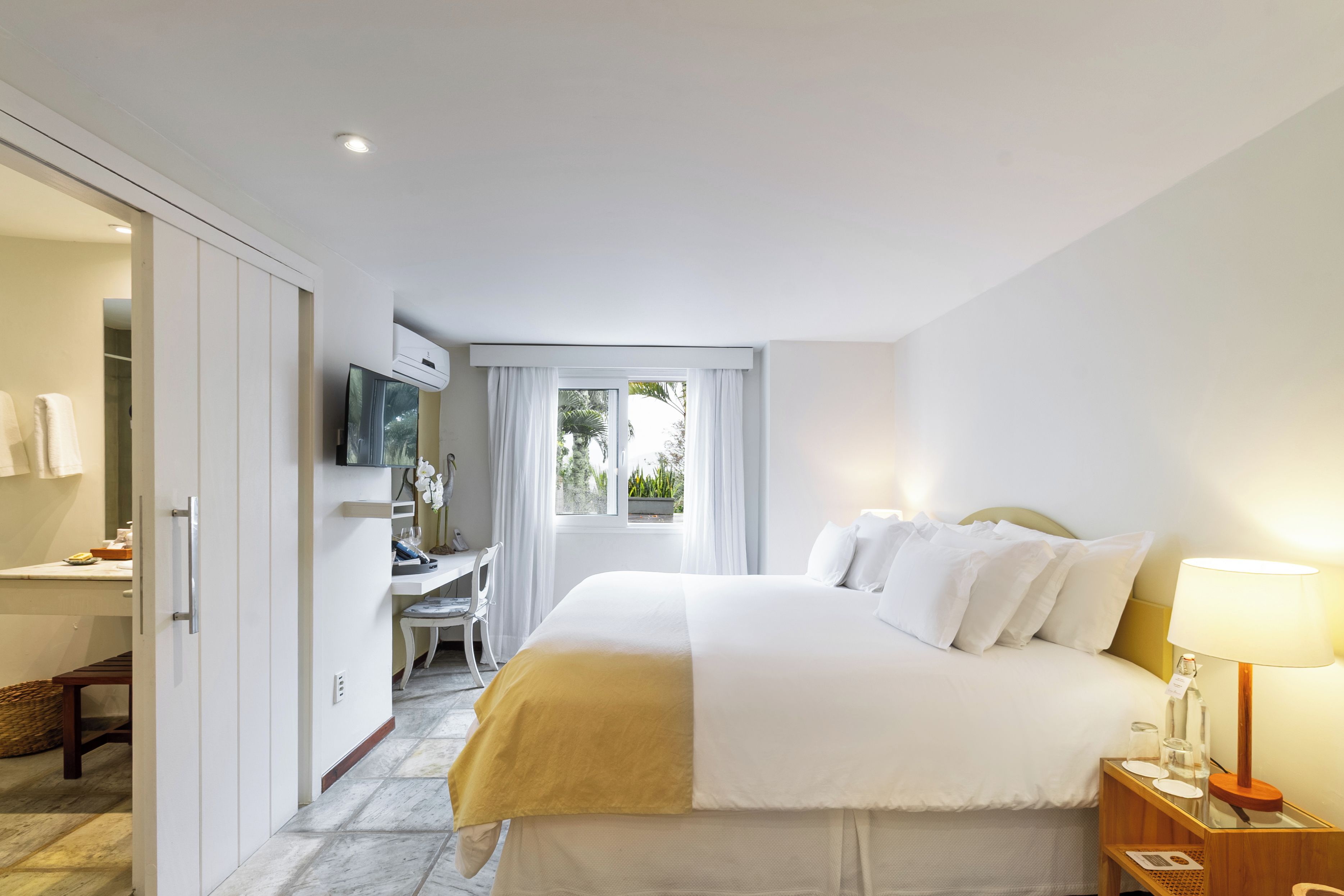 Habitación de hotel con cama, mesita de noche, lámpara y un escritorio con silla.